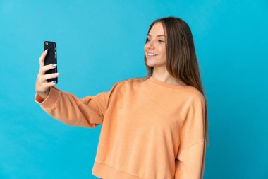 Young Lithuanian woman isolated on blue background making a selfie with mobile phone