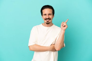 Mavi arka planda izole edilmiş genç beyaz adam mutlu ve dik duruyor.