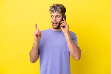 Sarı arka planda izole edilmiş cep telefonu kullanan genç beyaz bir adam bir fikri işaret ederek...