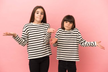 Pembe arka planda izole edilmiş küçük kız kardeşler ellerini ve omuzlarını kaldırırken şüpheye düşerler.