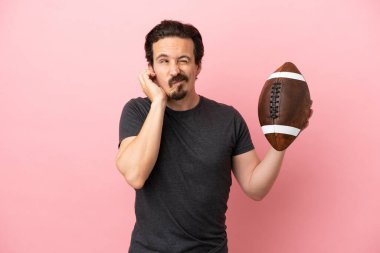 Genç beyaz adam rugby oynuyor. Pembe arka planda izole edilmiş. Hüsrana uğramış ve kulaklarını kapatmış.