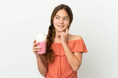 Beyaz arka planda izole edilmiş çilekli milkshake 'li küçük beyaz kız yukarı bakarken bir fikir düşünüyor.