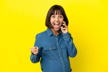 Sarı arka planda cep telefonu kullanan hamile kadın galibiyeti kutluyor.