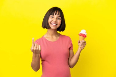Pregnant woman holding a cornet ice cream isolated on yellow background doing coming gesture