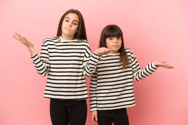 Küçük kız kardeşler pembe arka planda izole edilmiş mutsuz ve hayal kırıklığına uğramış çünkü bir şeyi anlamıyorlar.