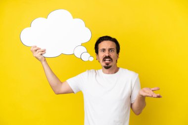Sarı arka planda izole edilmiş genç beyaz bir adam düşünme balonunu tutuyor ve hüzünlü bir ifadeyle