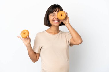 Genç melez hamile kadın beyaz arka planda izole edilmiş elinde donut ve mutlu bir kadın.