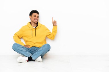 Young African American man sitting on the floor isolated on white background showing and lifting a finger in sign of the best