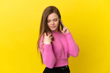İzole edilmiş sarı arka plan üzerinde cep telefonu kullanan genç bir kız omuz ağrısından muzdarip.