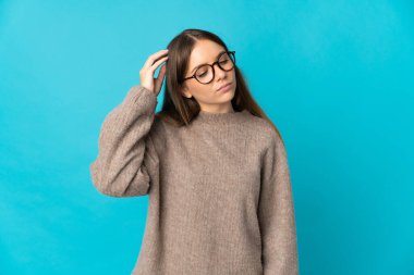 Genç Litvanyalı kadın mavi arka planda izole edilmiş. Kafasını kaşırken şüpheleri var.