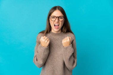 Genç Litvanyalı bir kadın mavi arka planda izole edilmiş. Kötü bir durum yüzünden hayal kırıklığına uğramış.