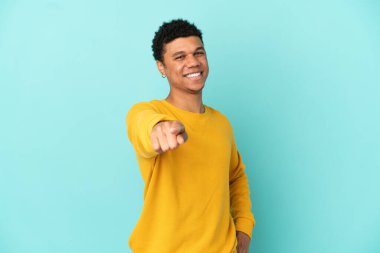 Young African American man isolated on blue background pointing front with happy expression