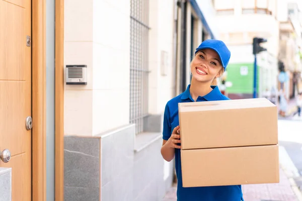 Young delivery woman at outdoors holding boxes with happy expression