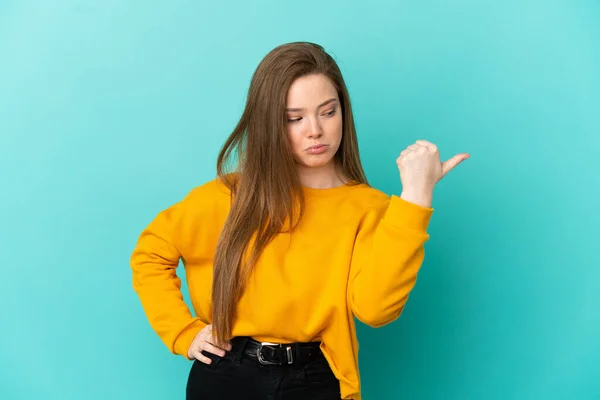 Adolescente Menina Sobre Isolado Fundo Azul Infeliz Apontando Para Lado — Fotografia de Stock