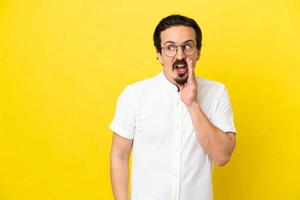 Young Caucasian Man Isolated Yellow Background Whispering Something Surprise Gesture — Stockfoto