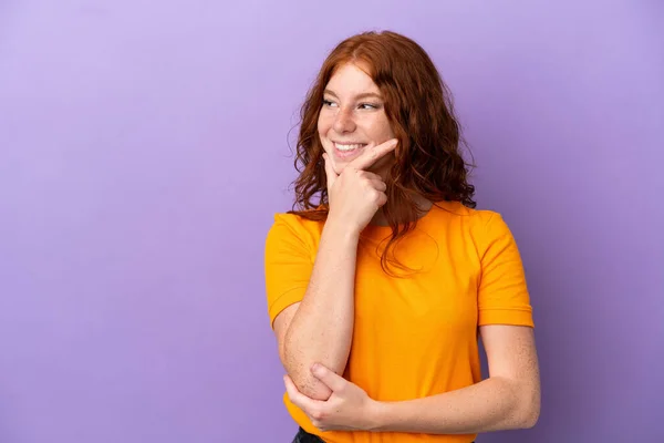 ティーンRedhead女の子上の隔離された紫色の背景見ますへザ側と笑顔 — ストック写真