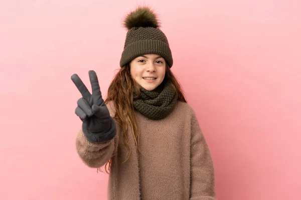 Dziewczynka Zimowym Kapeluszu Odizolowana Różowym Tle Uśmiecha Się Pokazuje Znak — Zdjęcie stockowe