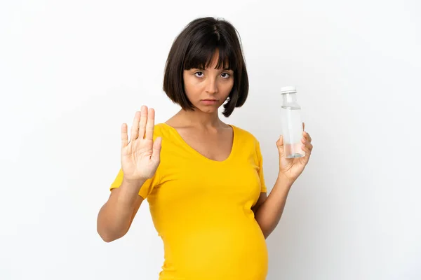 白い背景に孤立した水のボトルを持っている若い妊婦は停止ジェスチャーを作ります — ストック写真