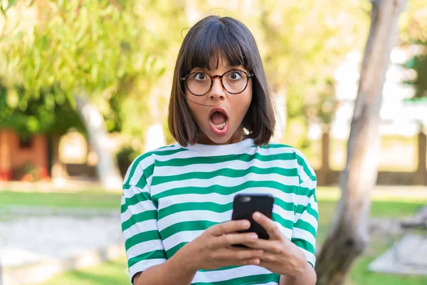 Young Brunette Woman Park Looking Camera While Using Mobile Surprised — Stock Photo, Image