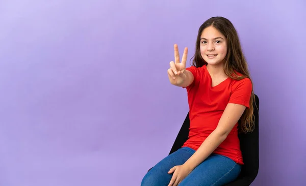 小さなCaucasian女の子座っています上の椅子に隔離された紫色の背景笑顔と示す勝利のサイン — ストック写真