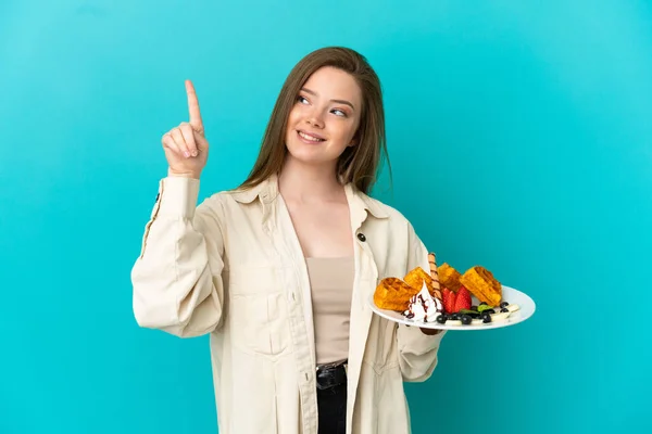 Adolescente Menina Segurando Waffles Sobre Isolado Fundo Azul Apontando Para — Fotografia de Stock