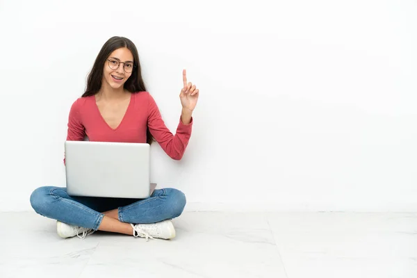 年轻的法国姑娘坐在地板上 她的笔记本电脑显示并举起了一个手指 这是最好的标志 — 图库照片