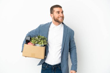 Beyaz arka planda izole edilmiş eşyalarla dolu bir kutuyu kaldırırken bir yandan yukarı bakarken bir fikir üreten genç beyaz bir adam hamle yapıyor.