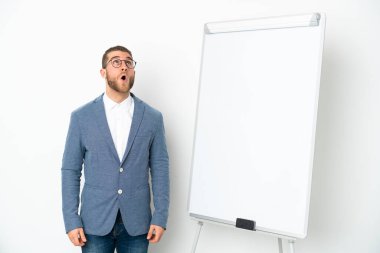 Beyaz arka planda izole edilmiş beyaz panoda sunum yapan genç iş kadını yukarı bakıyor ve şaşırmış bir ifadeyle