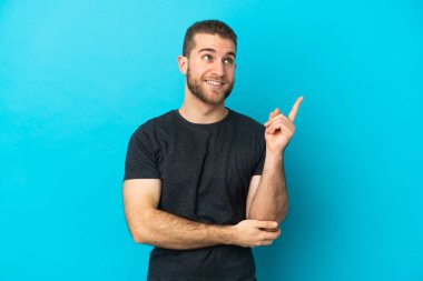 Mavi arka planda izole edilmiş yakışıklı beyaz adam harika bir fikre işaret ediyor.