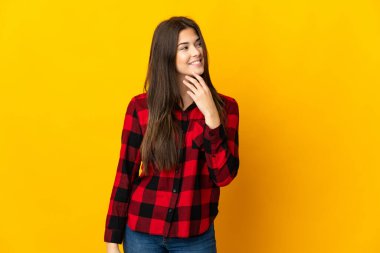 Genç Brezilyalı kız sarı arka planda izole edilmiş gülümserken yukarı bakıyor.