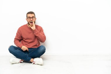 Genç yakışıklı adam yerde oturuyor ve ağzı açık bağırıyor.