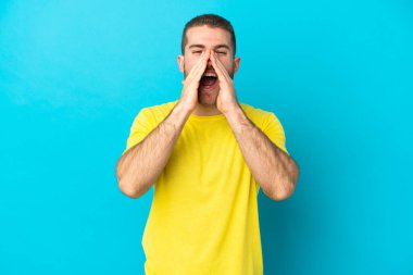 Genç beyaz adam mavi arka planda izole edilmiş bağırıyor ve bir şeyler söylüyor.