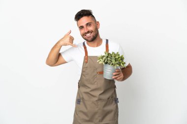 Bahçıvan beyaz arka plan üzerinde bir bitki tutuyor ve telefon jesti yapıyor. Bana geri dönüş işareti ver.