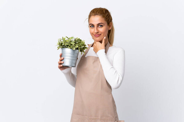Young blonde gardener woman girl holding a plant over isolated white background laughing