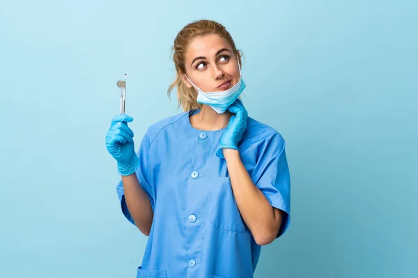 Mladá Žena Zubař Drží Nástroje Přes Izolované Modré Pozadí Myšlení — Stock fotografie