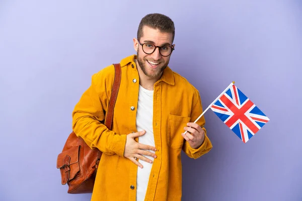 年轻的高加索人 拿着一面被紫色背景隔离的英国国旗 面带微笑 — 图库照片