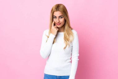 Genç Uruguaylı sarışın kadın izole pembe arka planda bir şey gösteriyor.