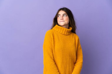 Mor arka planda izole edilmiş genç beyaz kadın yukarı bakarken şüpheleri var.