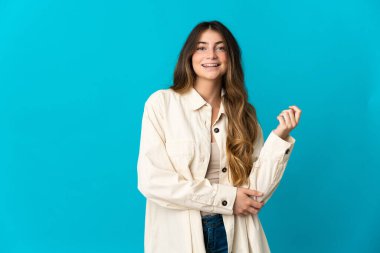 Mavi arka planda izole edilmiş genç beyaz kadın gülüyor.