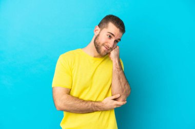 Mavi arka planda soyutlanmış, yorgun ve sıkılmış bir ifadeyle genç, beyaz bir adam.