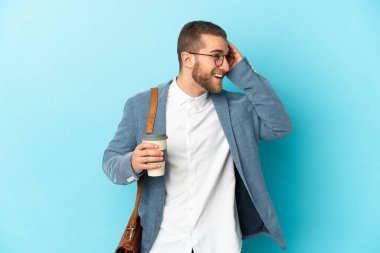 Kafkasyalı genç işadamı mavi arka planda izole edilmiş, gülümsüyor.