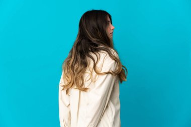 Kafkasyalı genç bir kadın mavi arka planda izole edilmiş ve arkasına bakıyor.