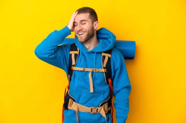 Sarı arka planda izole edilmiş büyük sırt çantalı beyaz bir dağcı. Çok gülümsüyor.