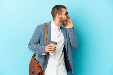 Kafkasyalı genç işadamı mavi arka planda izole edilmiş ve ağzı açık bağırıyor.