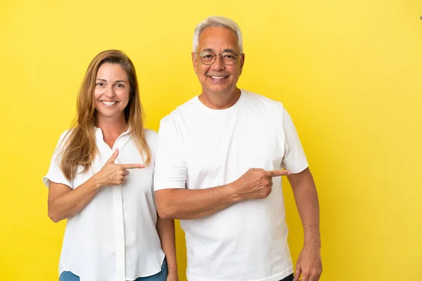 Middelaldrende Par Isolert Gul Bakgrunn Med Pekefinger Mot Siden Som – stockfoto