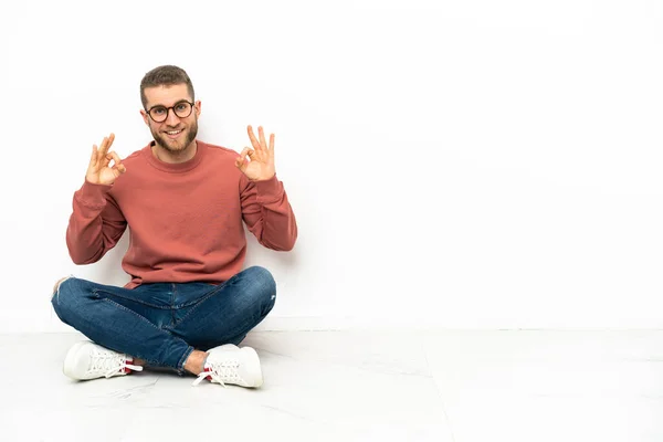 Mladý Pohledný Muž Sedící Podlaze Ukazující Znamení Prsty — Stock fotografie