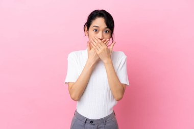 Pembe arka planda izole edilmiş genç Vietnamlı kadın elleriyle ağzını kapatıyor.