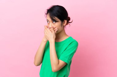 Genç Vietnamlı kadın pembe arka planda izole edilmiş ağzını kapatıyor ve yan tarafa bakıyor.