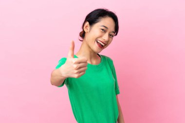 Genç Vietnamlı kadın pembe arka planda izole edildi. Başparmakları havada çünkü iyi bir şey oldu.