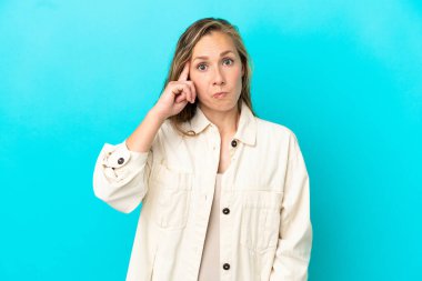 Kafkasyalı genç bir kadın mavi arka planda izole edilmiş bir fikir düşünüyor.